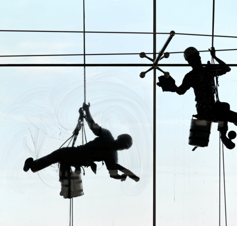 Two professional window cleaners suspended by rope access systems clean the exterior glass of a high-rise building, ensuring a spotless finish with specialized equipment.