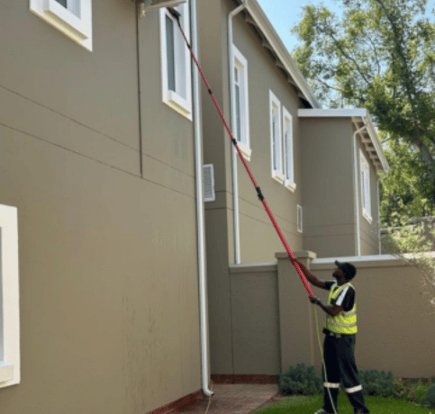 A man cleaning a residential window with purified water using a water-fed pole.
