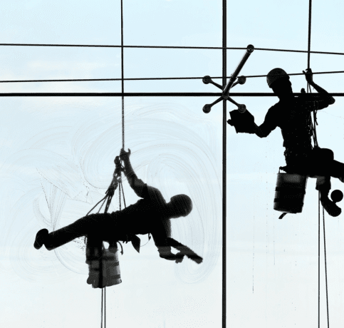 Window cleaners using rope access to clean the exterior windows of a high-rise building.